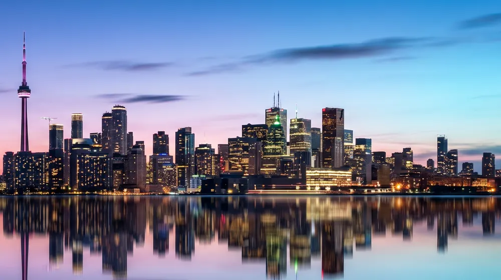 Toronto skyline with the CN Tower at dusk, lit up and reflected in the lake